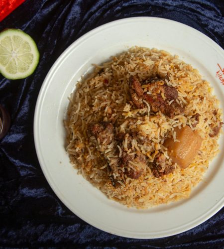 Delicious biryani with tender lamb pieces served on a white plate garnished with spices and lime.